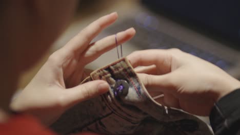 a woman with a tattoo sewing a piece of button on a faded jeans