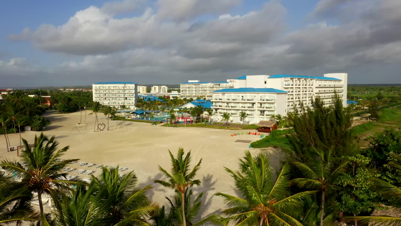Aerial establishing pullback of beachfront hotel and palm lined road in Margaritaville, Cap Cana Juanillo Beach Dominican Republic