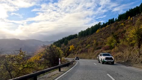 a vehicle travels a winding rural road through autumn hills and farmland near queenstown, new zealand, under partly cloudy skies with scenic mountain views