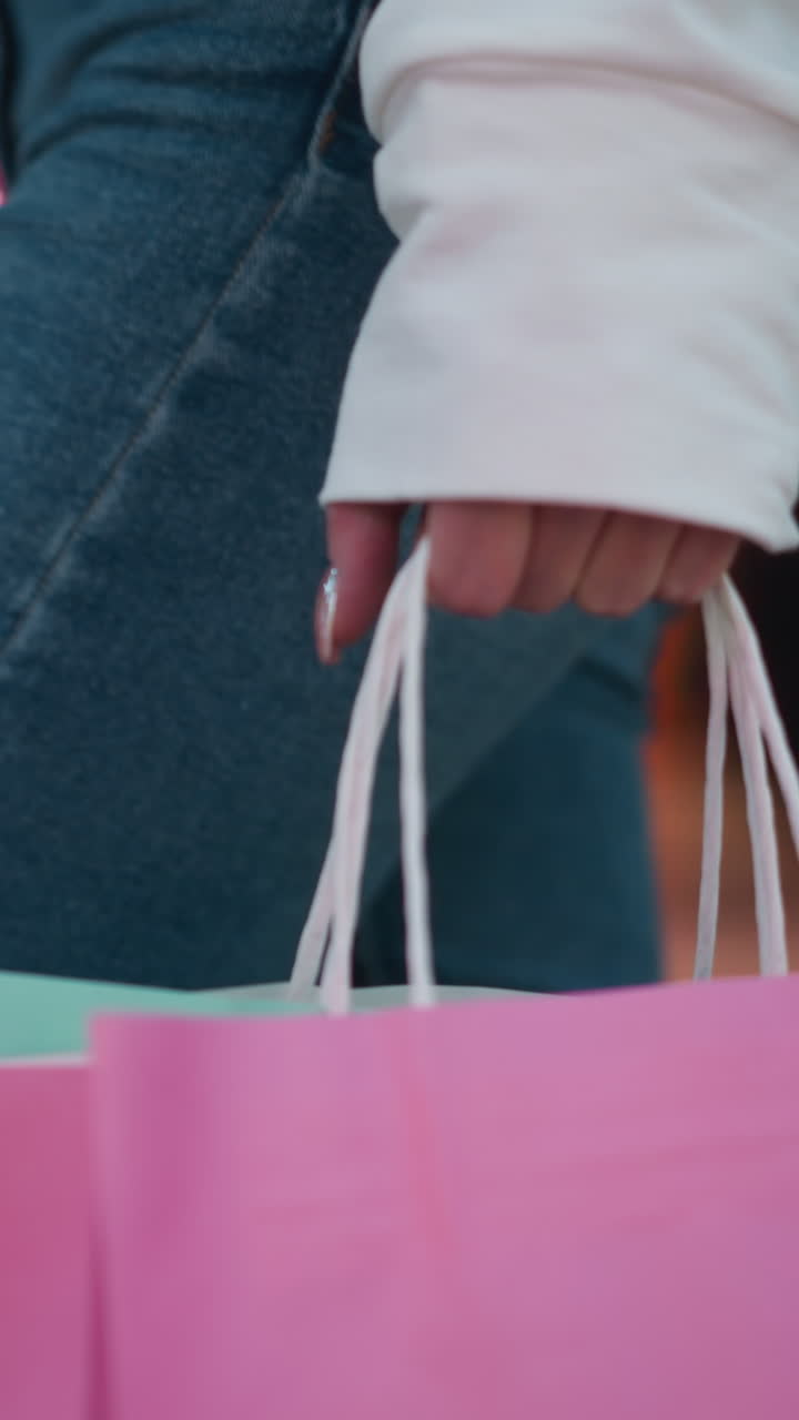 핑크색 쇼핑 가방은 은 손으로 들고 있으며, 민트색 가방은 약간 눈에 띄고, 활기찬 쇼핑몰 배경에 마네킨 디스플레이, 유리 및 불빛의 흐릿한 반사 등이 있습니다.