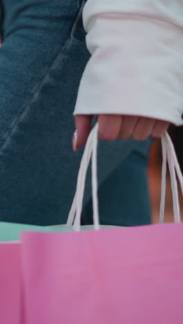 bolsa de compras rosada sostenida en la mano pulida con bolsa de color menta ligeramente visible, puesta contra el vibrante fondo del centro comercial con exhibición de maniquíes, reflejos borrosos de vidrio y luces