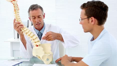 Mature-doctor-speaking-to-his-patient-about-model-of-spine
