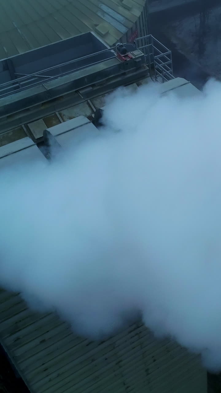 Working premises at elevator plant, thick pipes letting out heavy thick smoke. Flying above the tops of granary silo at the backdrop of grey weather. Vertical video