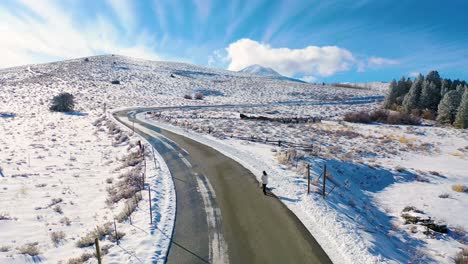 2020---Antenne-Einer-Geräumten-Frau,-Die-Hund-Entlang-Der-Schneebedeckten-Bergstraße-In-Den-östlichen-Sierra-Nevada-Bergen-In-Der-Nähe-Der-Mammoth-Lakes-Kalifornien-Geht-1