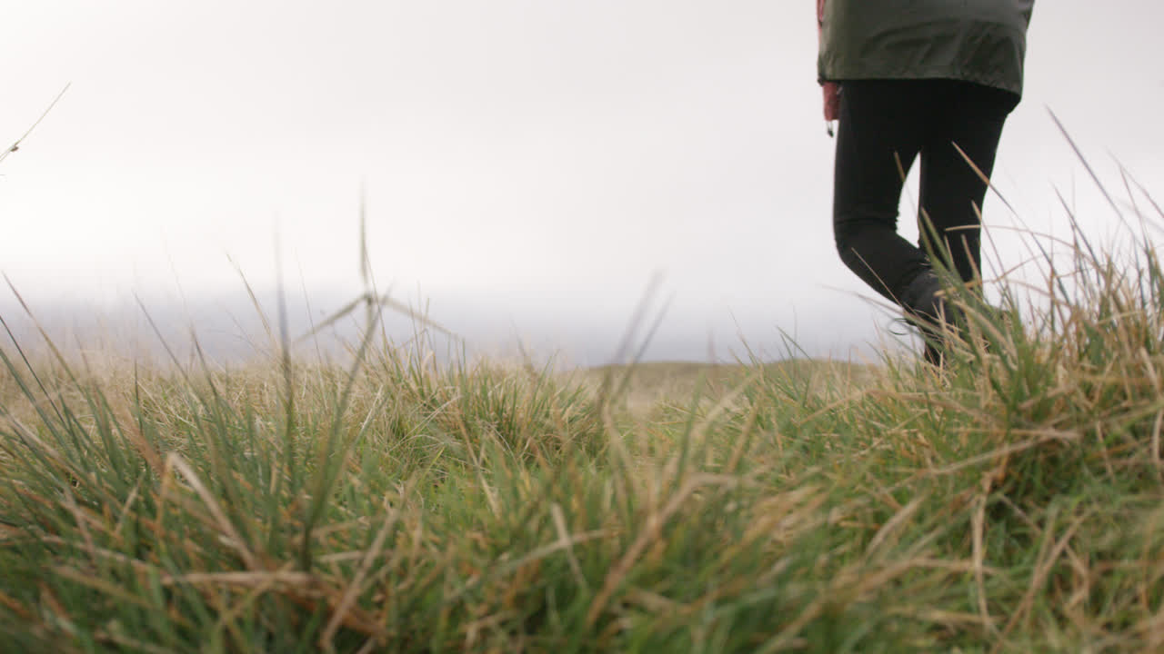 풍력 터빈이 있는 영국 시골과 언덕을 가로지르는 여성 산책