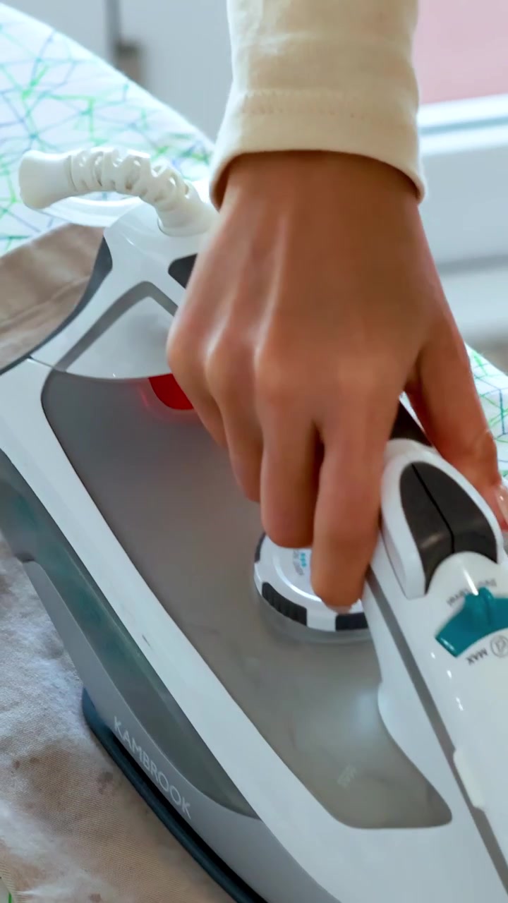 Close-up of hand using steam iron and spray to smooth wrinkles from trousers in daylight.