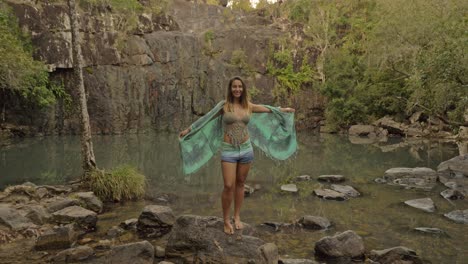 Sexy-Junge-Kaukasische-Frau,-Die-Einen-Schal-Trägt,-Der-Die-Hand-Hebt-Und-In-Den-Himmel-Schaut---Wasserloch-Bei-Cedar-Creek-Falls-In-Australien