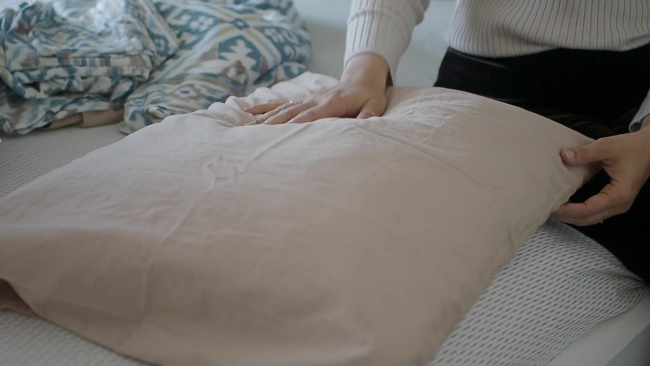 Woman Putting a Pillowcase on a Pillow on a Bed