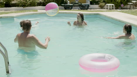 kaukasische familie, die an einem sommertag im schwimmbad ball spielt