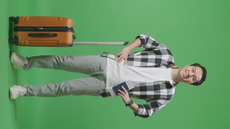 full body of asian male traveler with luggage and passport standing with arms akimbo and smiling in the green screen background studio