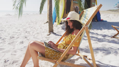 Mujer-Caucásica-Sentada-En-Una-Tumbona-Y-Usando-Su-Computadora-Portátil-En-La-Playa