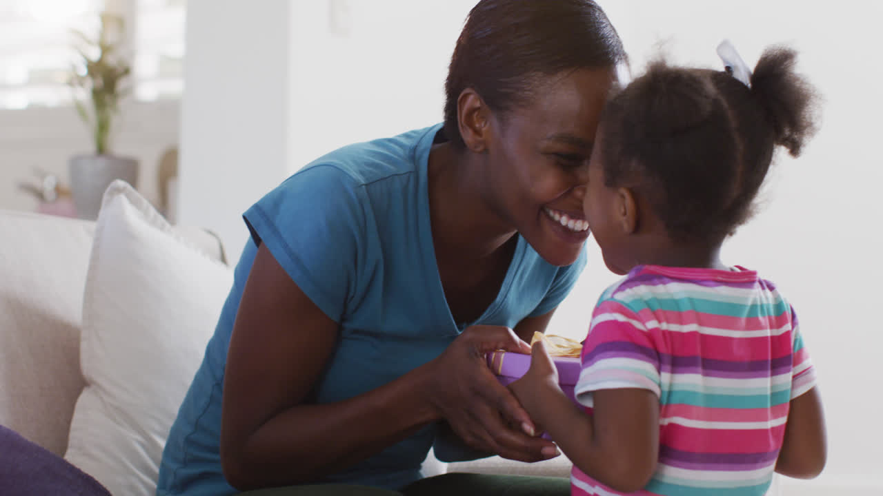 Happy african american mother and daughter sitting on sofa and touching foreheads