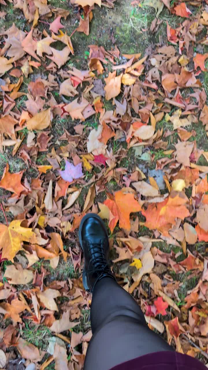 Walking though colorful fall leaves on ground wearing black boots - looking straight down