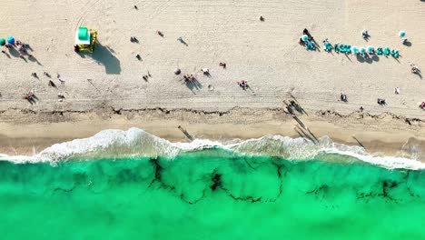 Die-Küste-Von-South-Beach-Miami-Mit-Kleinen-Wellen,-Die-Ans-Ufer-Krachen,-Mit-Einigen-Sonnenschirmen-Und-Menschen-Am-Strand