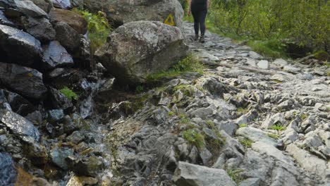 Female-hiker-walking-rocky-path-along-mountain-streamlet,-Alpe-Ventina