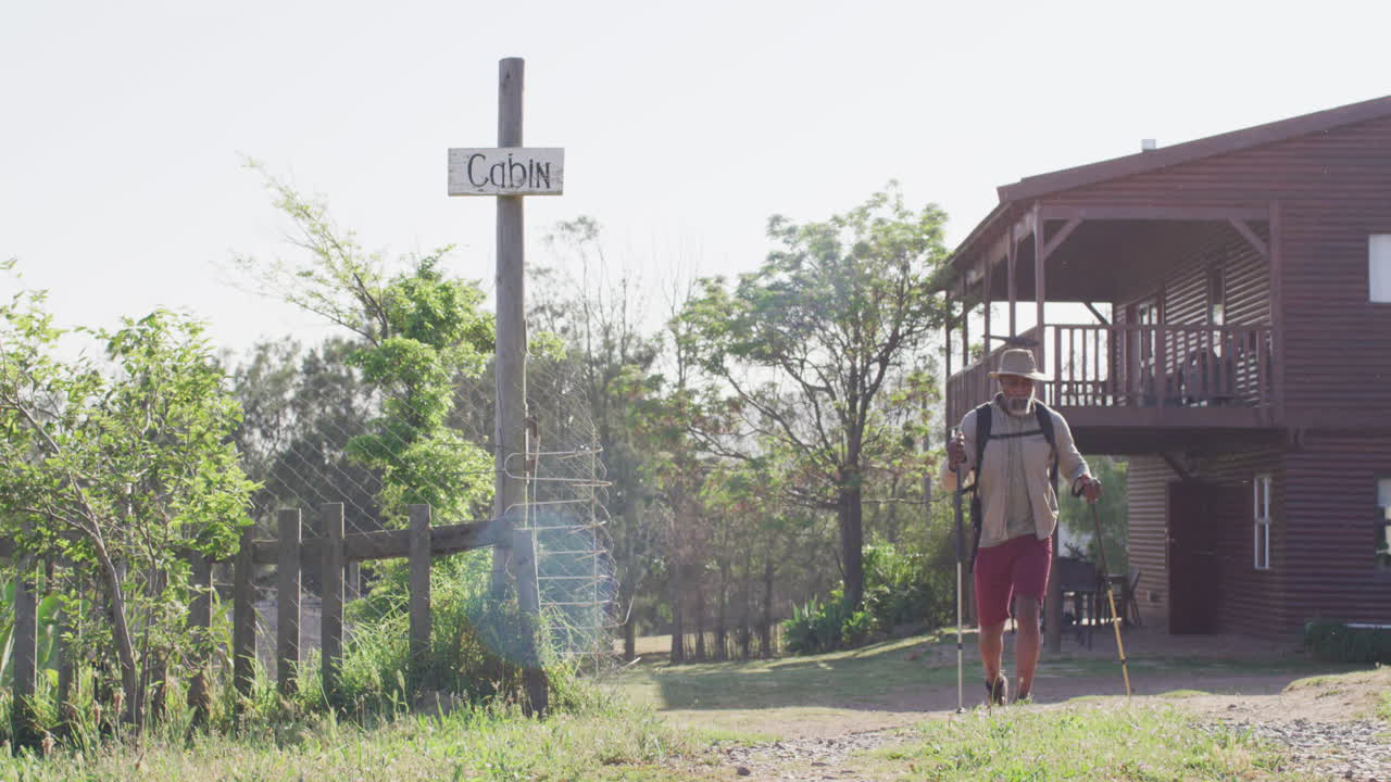 Senior african american man hiking with trekking poles on sunny day, slow motion