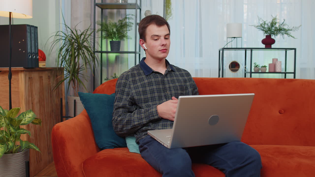 hombre sentado en el sofá de casa, mirando a la cámara, haciendo una llamada de videoconferencia con amigos o familiares
