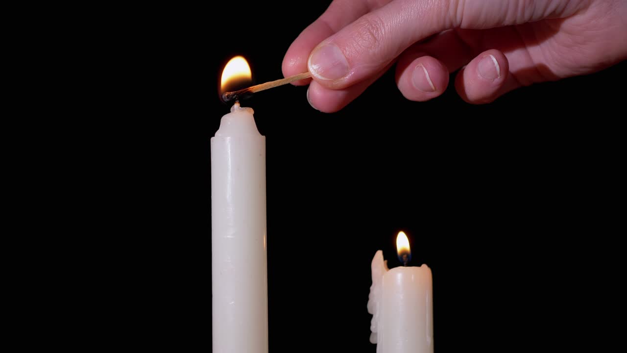 la mano de la mujer enciende dos velas de parafina usando un fósforo sobre un fondo negro. 4k