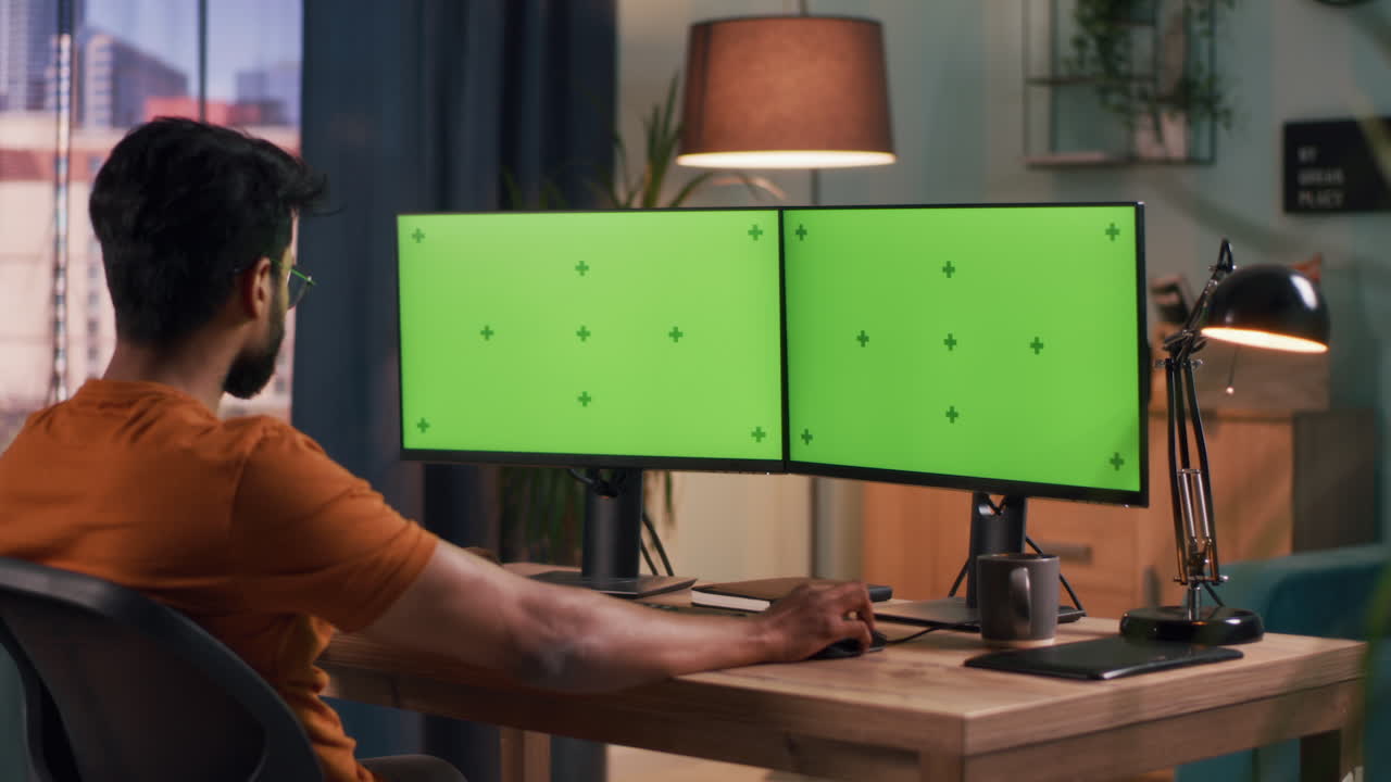 Person Working on Dual Monitor Setup with Green Screen
