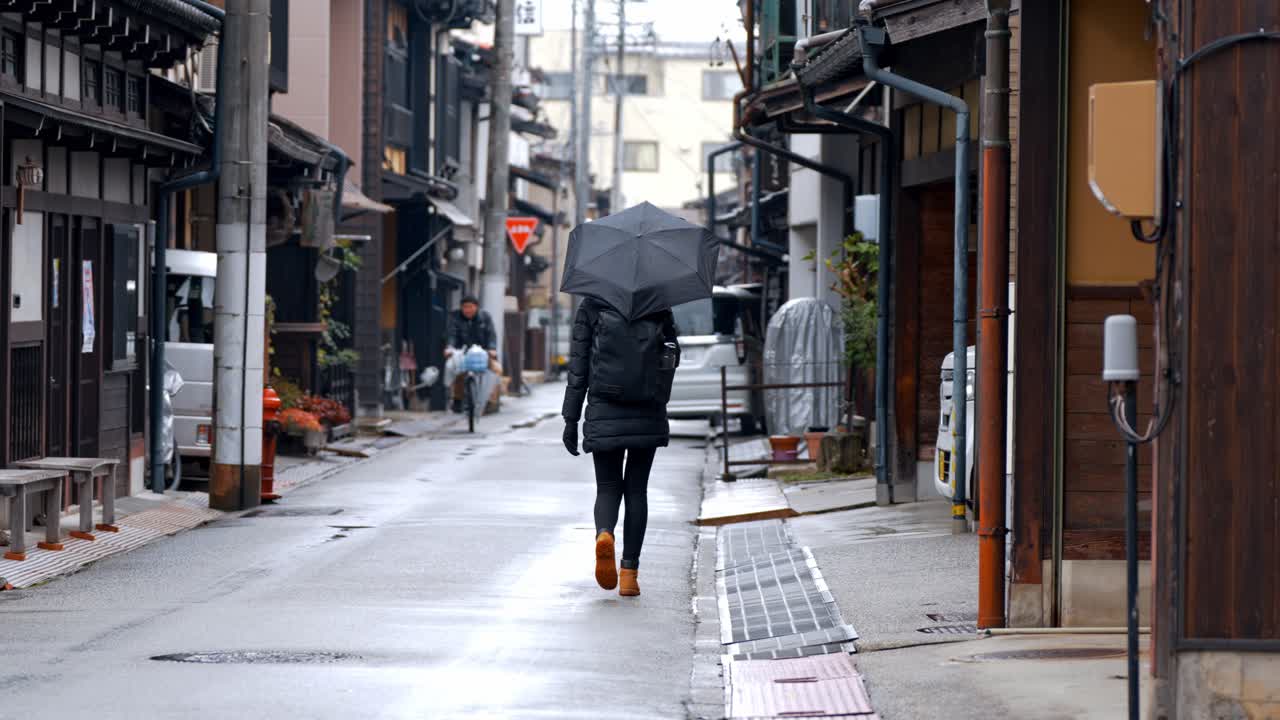 A woman strolls through the charming streets of Takayama on a rainy day, her umbrella shielding her from the gentle drizzle.