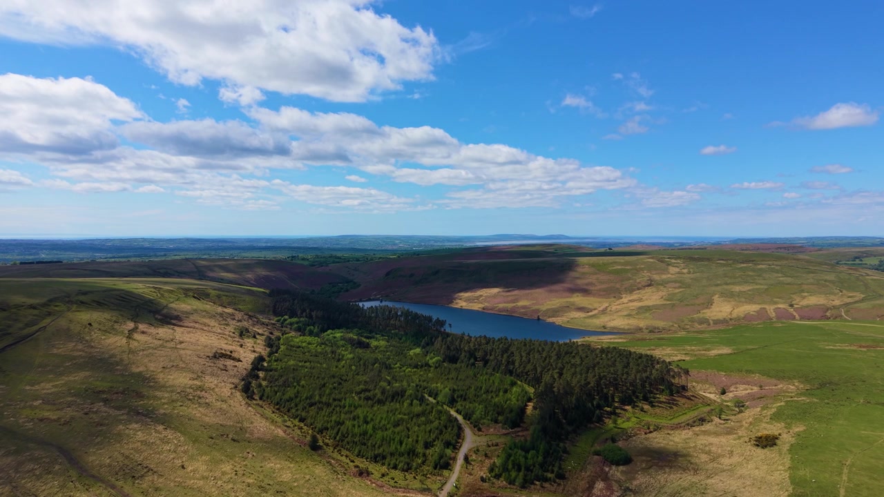 Dramatisk og vidstrakt luftfoto av landskapet i Sør-Wales, Storbritannia, med det nærliggende Lliw-reservoaret mot en dramatisk himmel, omgitt av skog og åpent gressland. 4K.