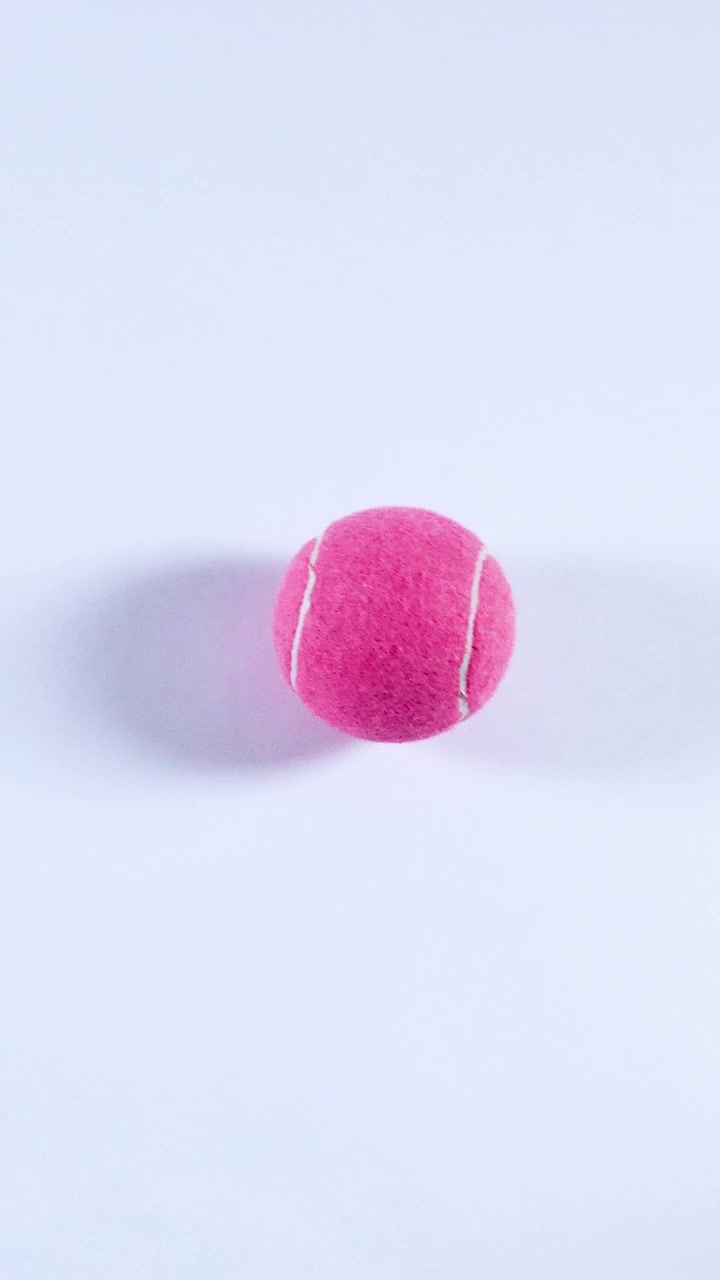 A pink tennis ball rolls across a surface