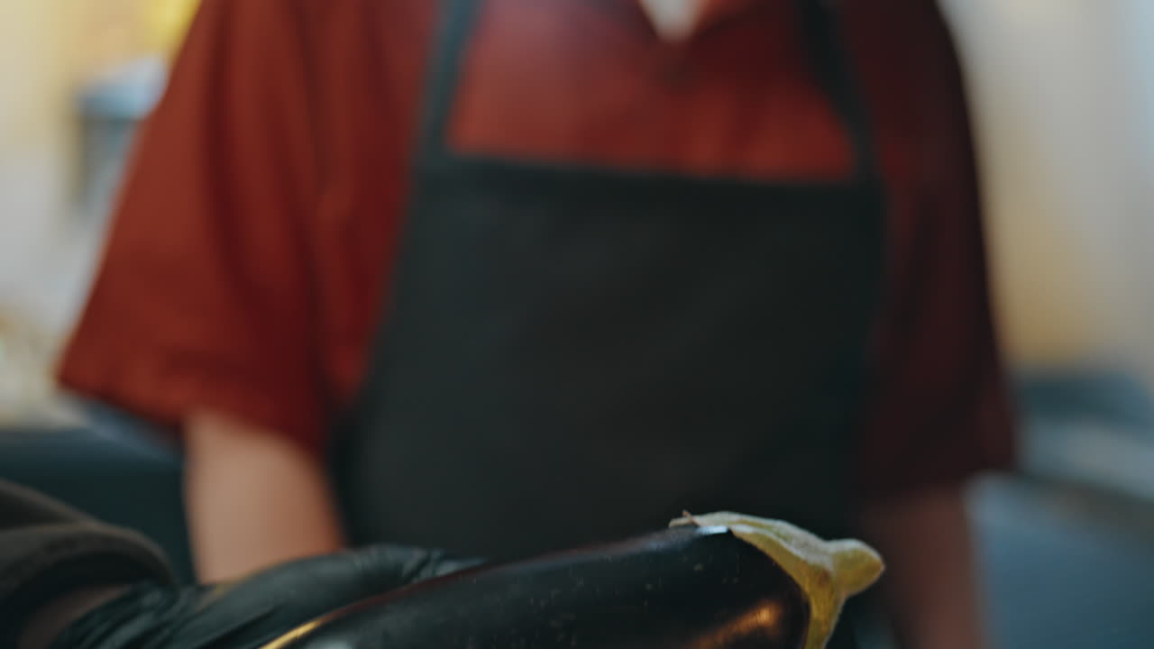 Gloved hands holding eggplant in kitchen teaching young woman to prepare closeup