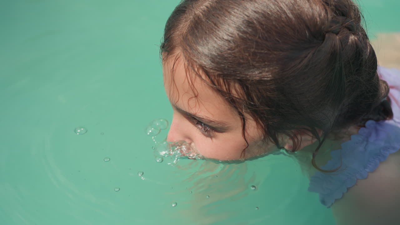 Young Girl Blowing Bubbles In Pool, CloseUp Side Profile With Braided Hair, Turquoise Water, Gentle Splash And Summer Sunlight, Candid Backyard Moment Showing Concentration And Playful Innocence