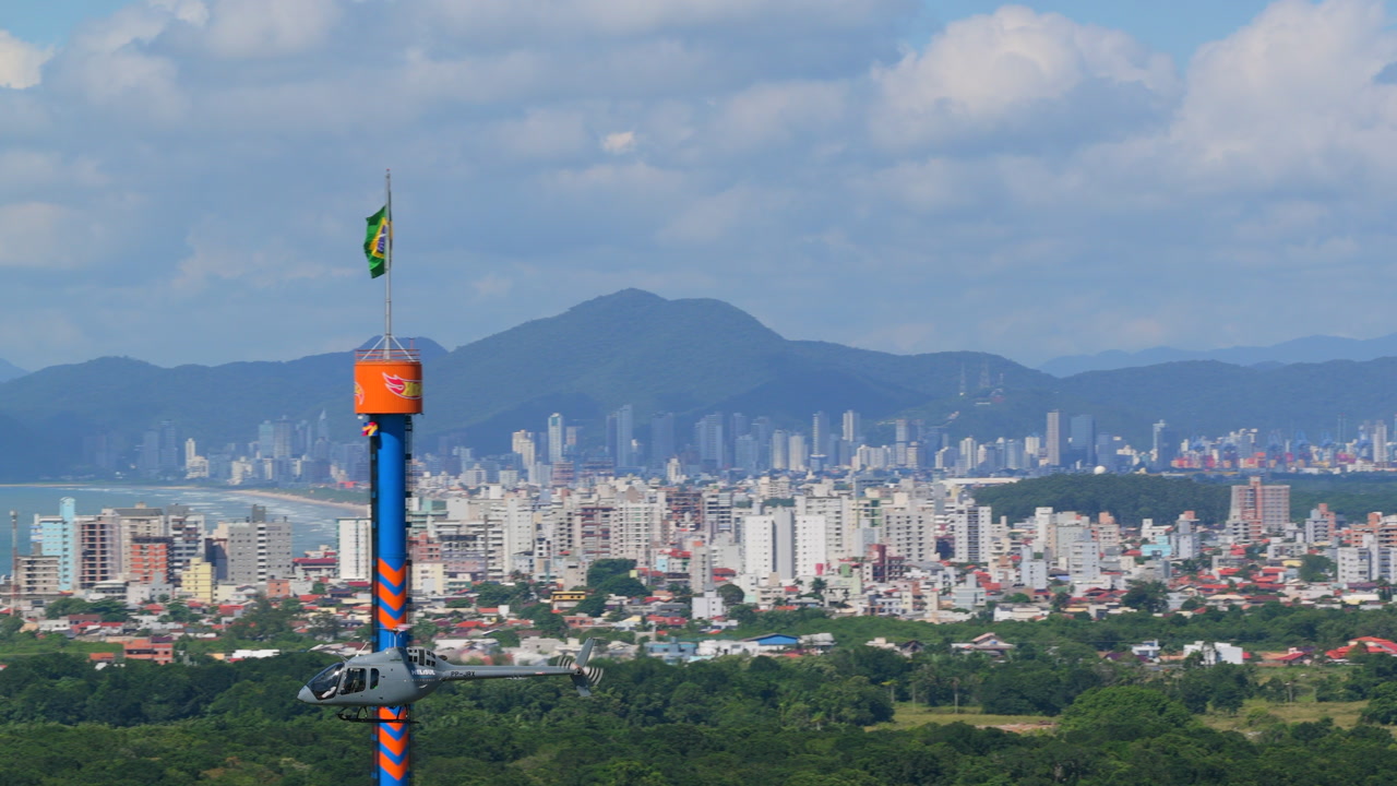 Telephoto aerial shot of helicopter landing at Beto Carrero World in Penha with green hills background.