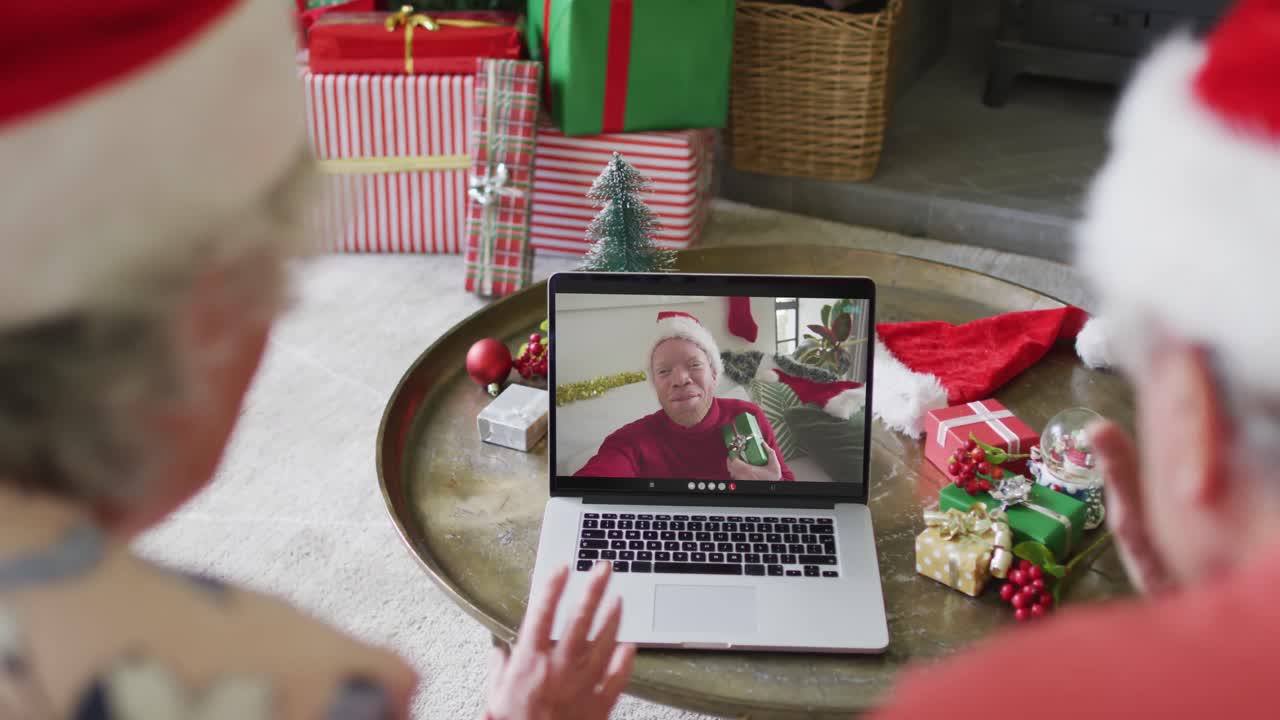 pareja caucásica de alto nivel con sombreros de santa usando una computadora portátil para una videollamada de navidad con un hombre en la pantalla