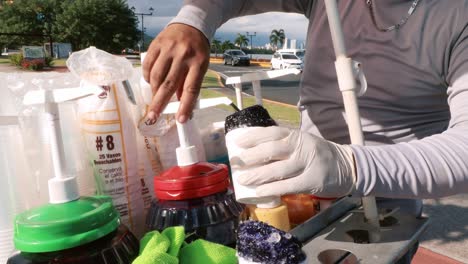 Man working on the streets with a cart making a cold refreshing shaved ice also known as a raspado during a hot day in the summer tropical climate of Panama City's promenade of the Causeway of Amador