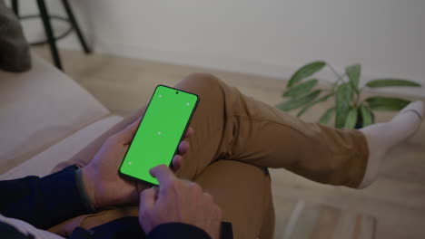 man sitting on his sofa in conversation, receives notification on his smartphone, green screen