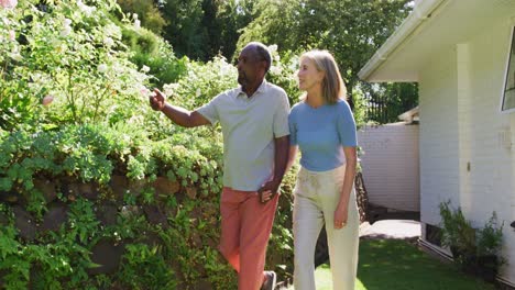 diverse senior couple walking in their garden in the sun holding hands and talking