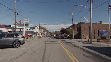 Wilson,-NY,-USA,-October-2021:-A-typical-street-in-a-small-American-town,-as-seen-from-the-rear-window-of-a-passing-car.-On-the-sides-there-are-houses-and-small-shops,-typical-US-road-signs