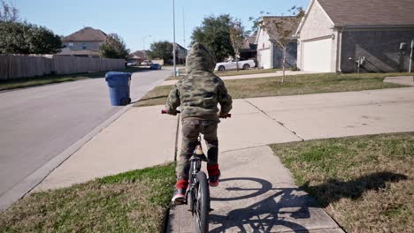 a young boy rides his bike on a sidewalk through his neighborhood in 4k slow speed