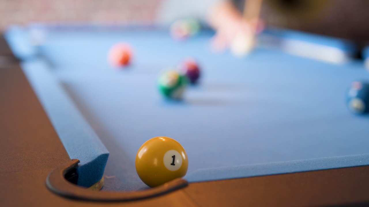 Yellow billiard ball rolls into corner pocket on blue felt table, shallow focus, natural lighting