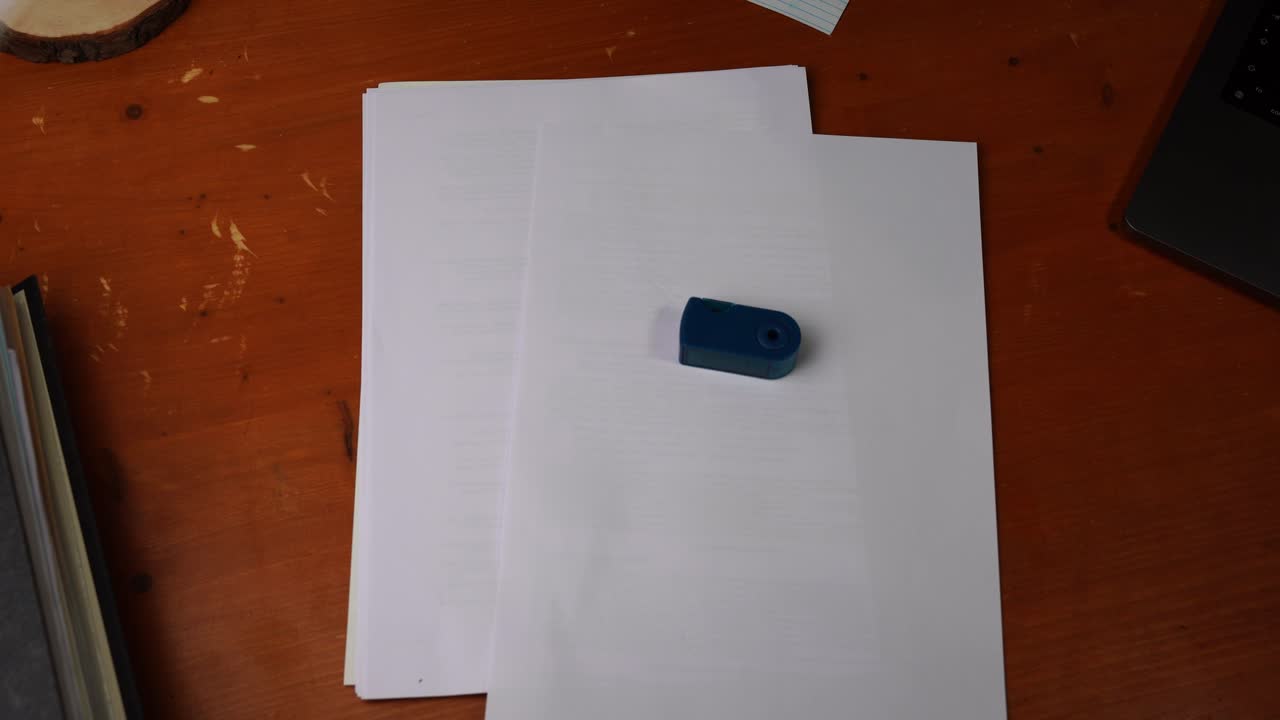 blue sharpener is placed on a piece of paper on a desk and again by a hand