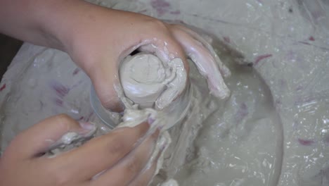 Hands working clay on potter's wheel. Potter shapes the clay product.