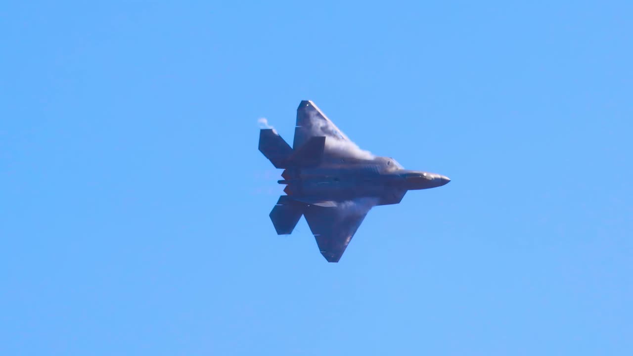 An F-22 Raptor executes dynamic aerial maneuvers against a clear blue sky, showcasing its agility and speed