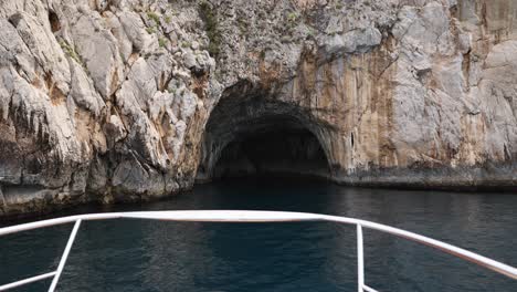 boat approaching ocean cliff cave on coast of capri island, italy