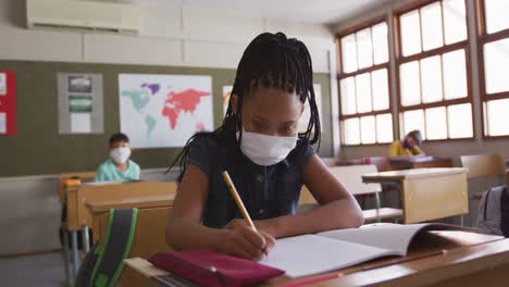 Mädchen-Mit-Gesichtsmaske-Niest,-Während-Sie-In-Der-Schule-Auf-Ihrem-Schreibtisch-Sitzt