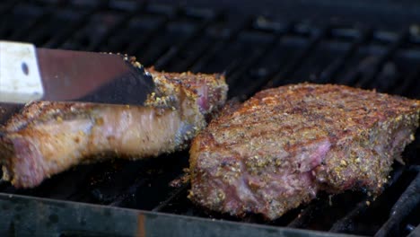 a pair of meat tongs turn a nearly cooked juicy rib eye steak on a grill and slides it a bit in slow motion