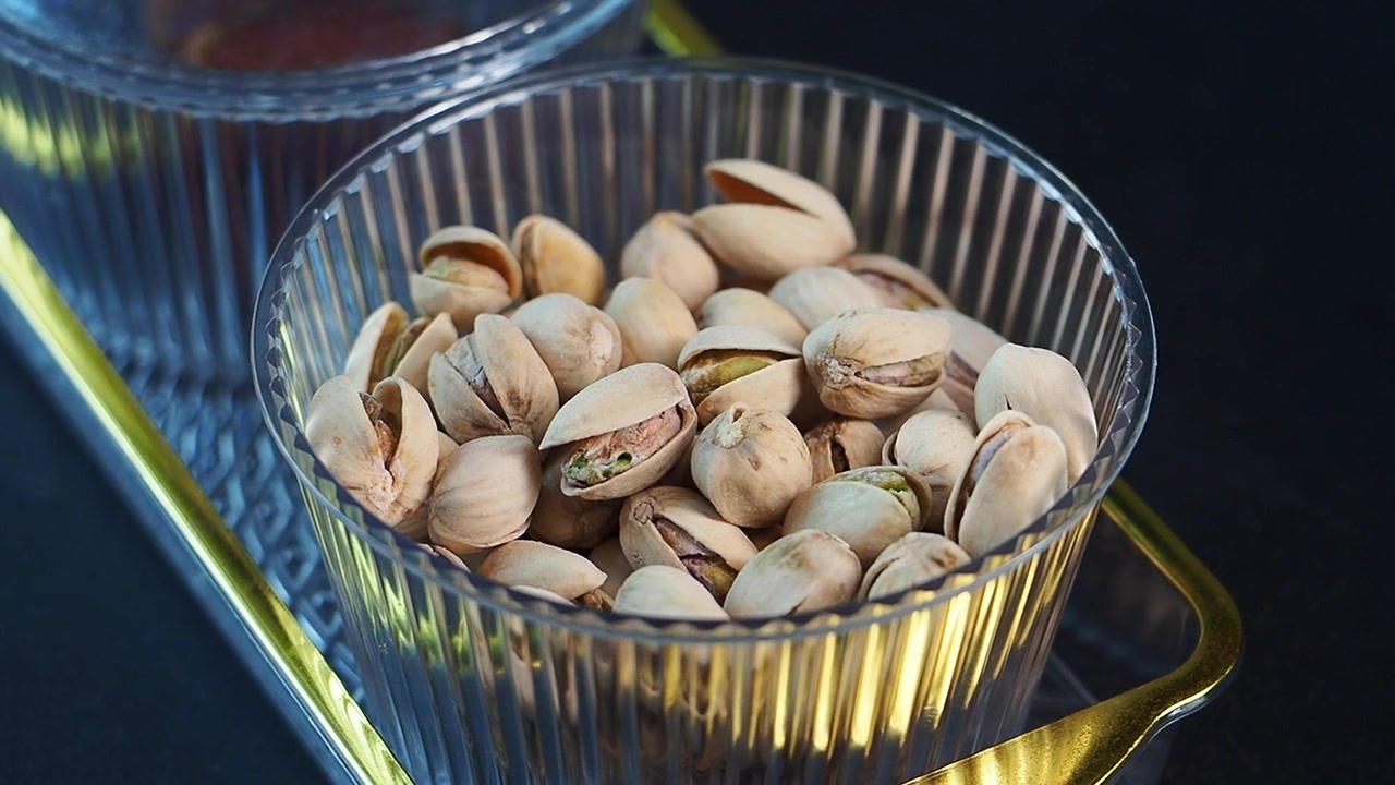 Primo piano di pistacchi in una ciotola trasparente su un vassoio dorato