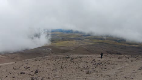 a rocky volcanic landscape on cotopaxi volcano, ecuador, under a cloudy sky with barren slopes, man hikes up solo