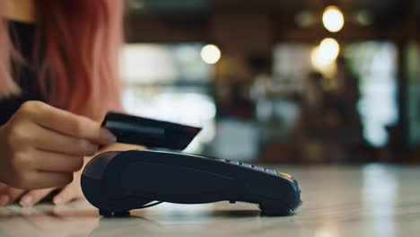 a close-up view of a person making a contactless payment with a credit card at a point of sale device in a modern cafe setting