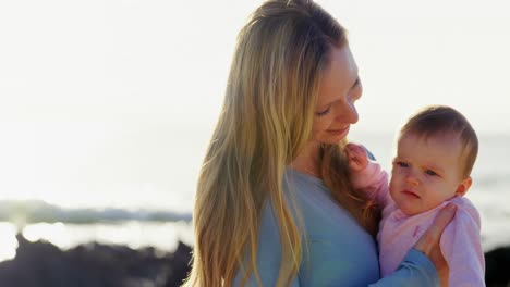 Side-view-of-mid-adult-caucasian-mother-kissing-her-baby-at-beach-on-a-sunny-day-4k