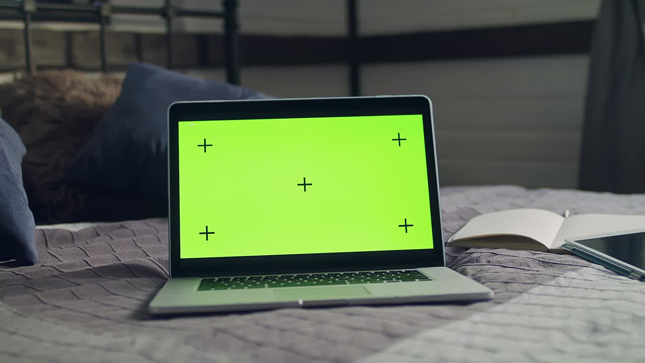 The laptop, notebook with green screen and tracking markers. Mobile tablet lying on the bedspread.