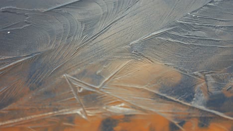 on the surface of a shallow lake with a rocky bottom, abstract patterns form on the thin, transparent ice