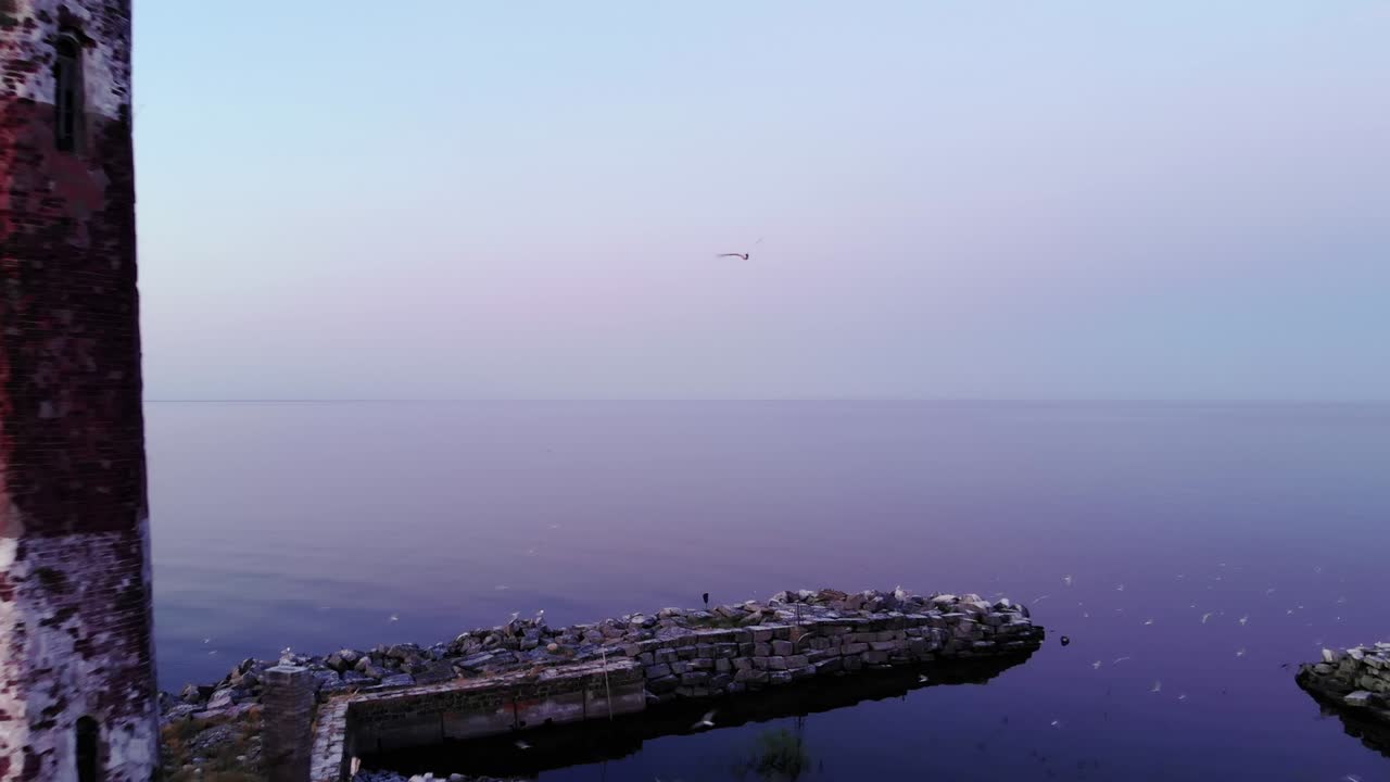 Cinematic aerial shot of small island with old lighthouse, camera fly back