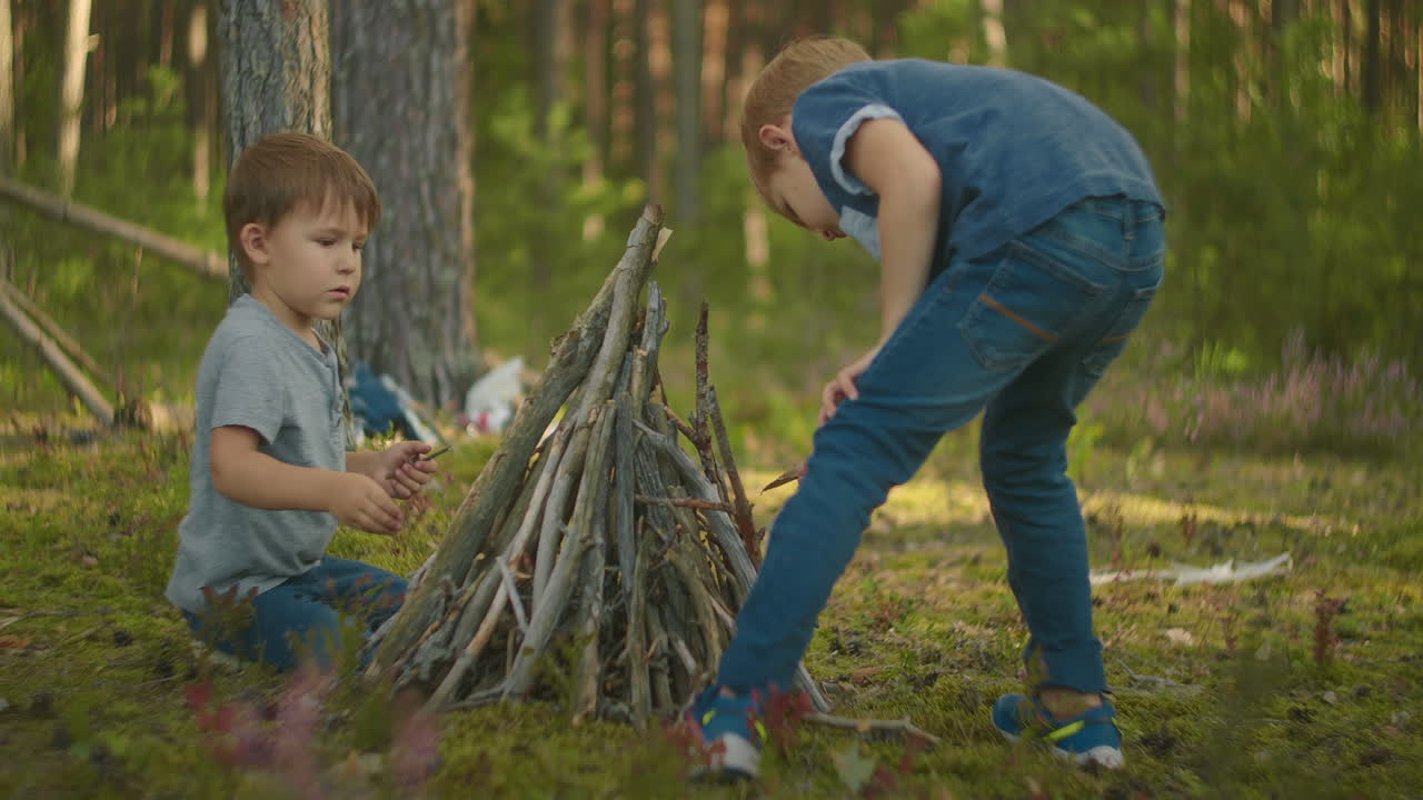 dos niños ponen palos en un fuego en el bosque durante una caminata. los niños en el bosque se preparan para encender un fuego y ponen palos juntos